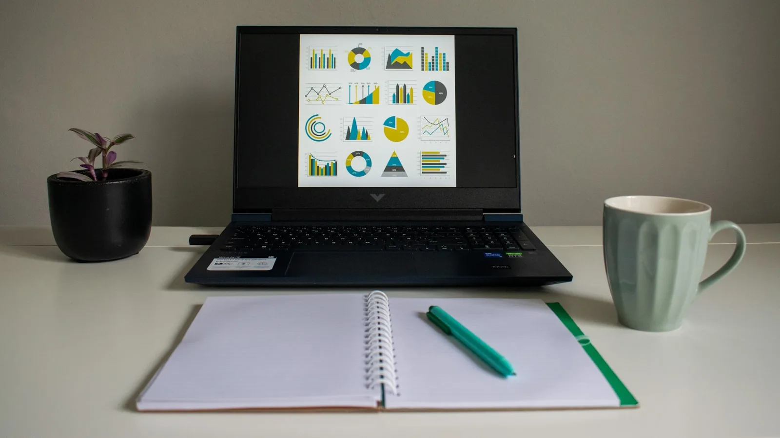A laptop displaying charts beside an open notebook